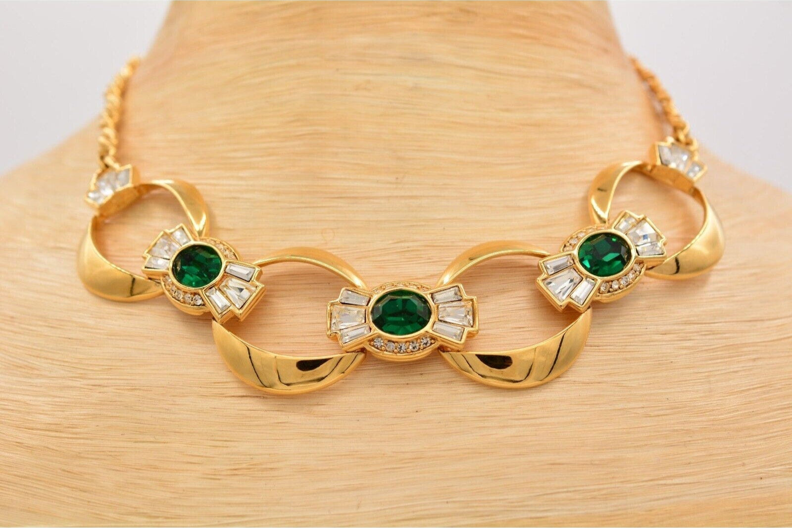 Close up view of a shiny old colored vintage Givenchy collar necklace with large emerald colored crystals surrounded by clear baguette crystals on a light colored neck