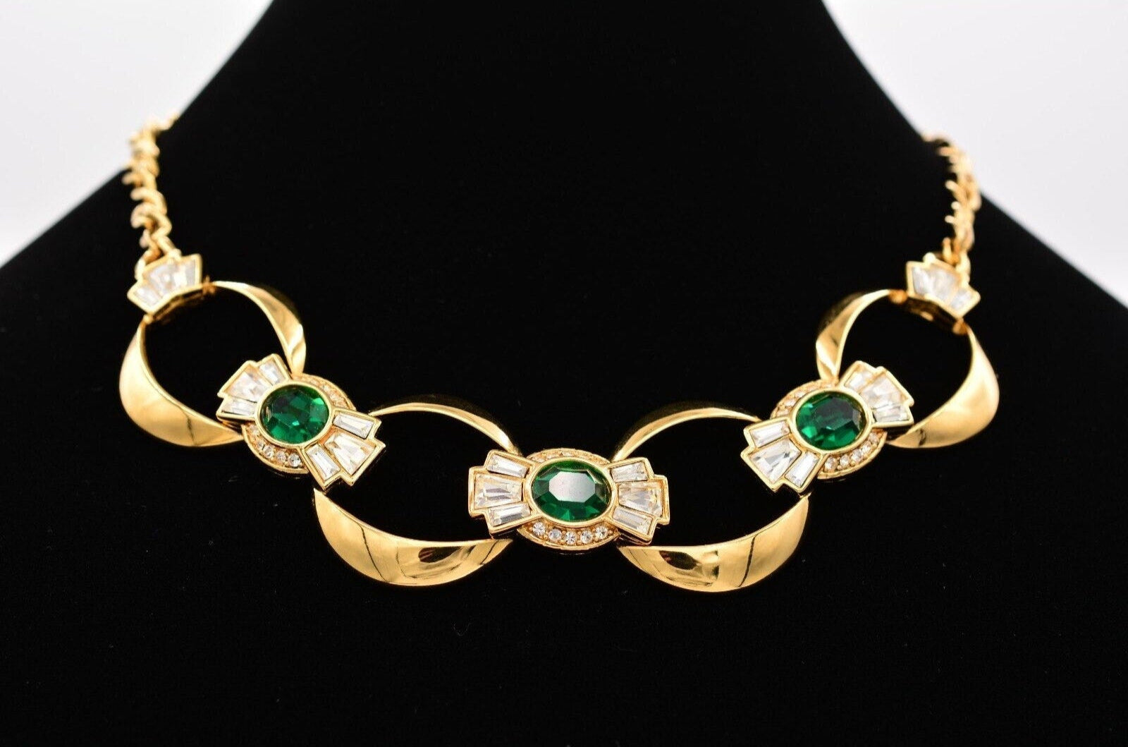 Close up view of a shiny old colored vintage Givenchy collar necklace with large emerald colored crystals surrounded by clear baguette crystals