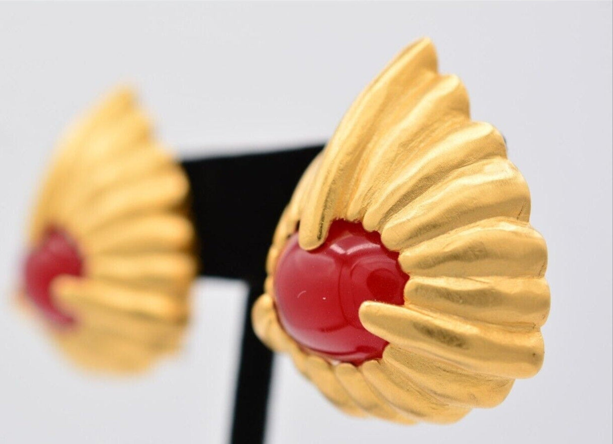 Close view of of the left brushed gold vintage Givenchy earring with bright red cabochon in the center on a black velvet stand with the right earring blurred in the background