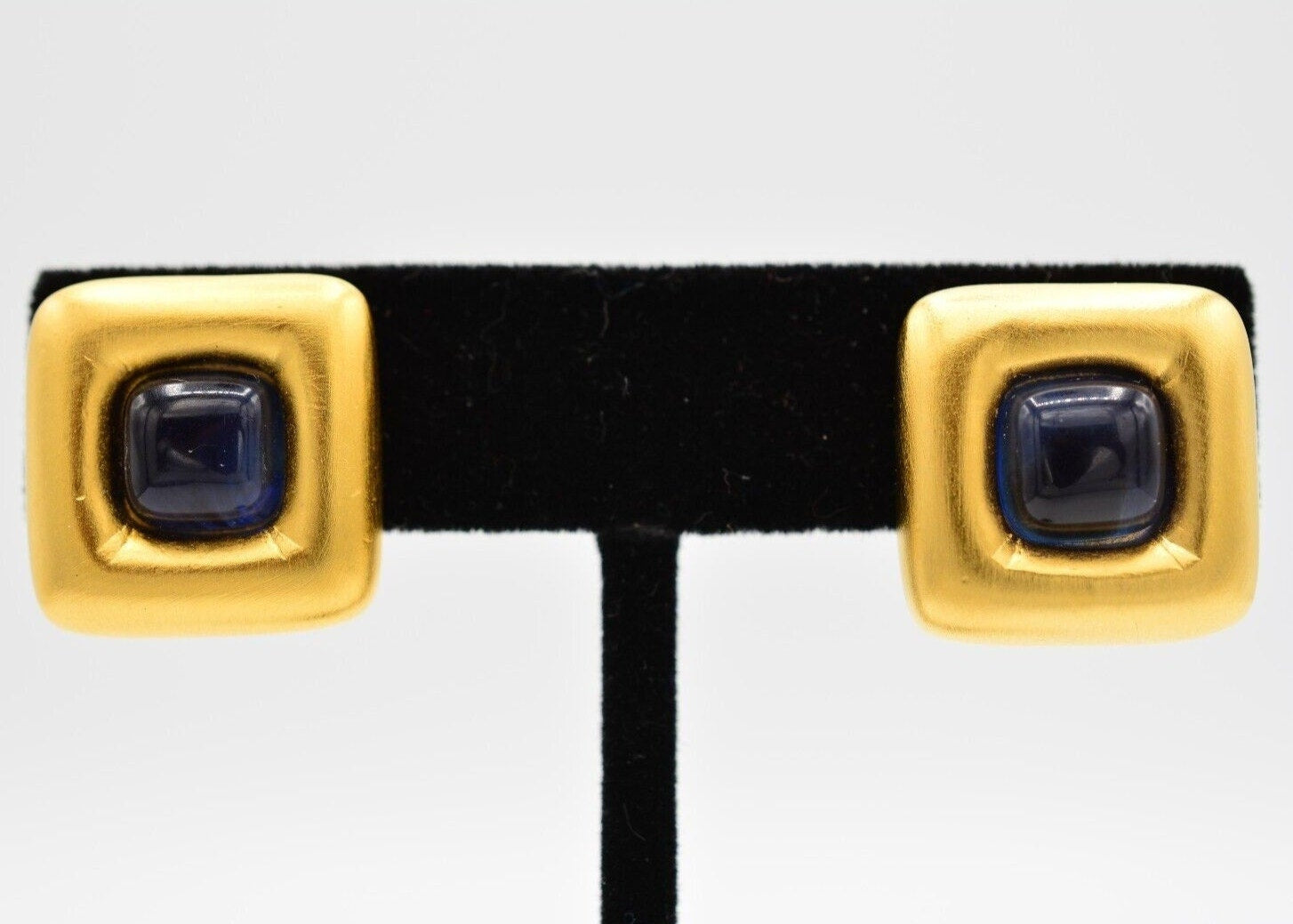 View of a pair of vintage Givenchy brushed gold clip on earrings with dark blue cabochons in the center on a black velvet stand