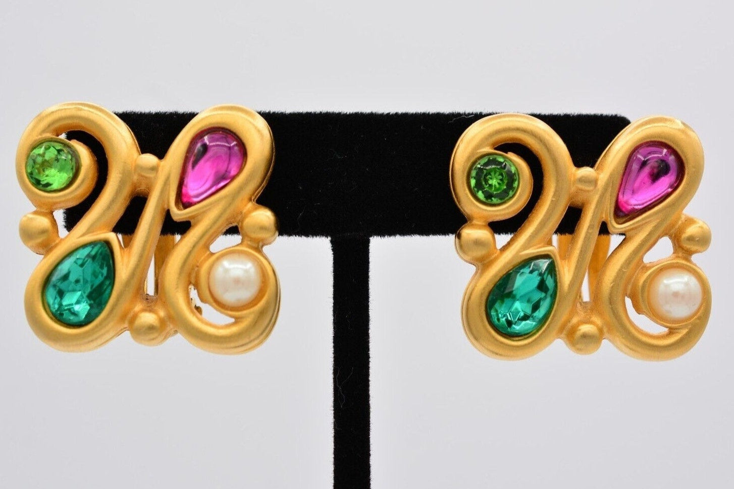 Vintage brushed gold Givenchy earrings with colorful pink green and blue crystals cabochons and a pearl front view on an earring tree