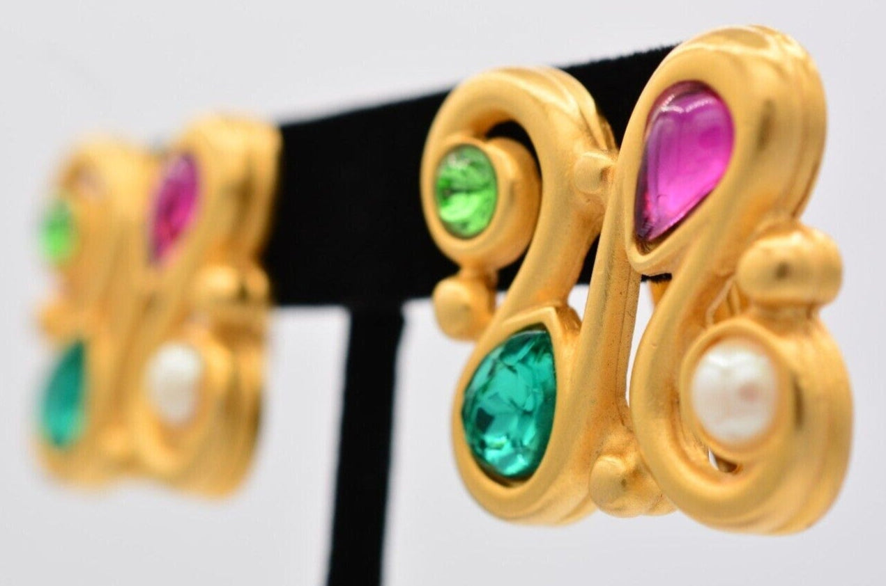 Vintage brushed gold Givenchy earrings with colorful pink green and blue crystals cabochons and a pearl close up side view of one earring on an earring tree while the other is blurred in the background