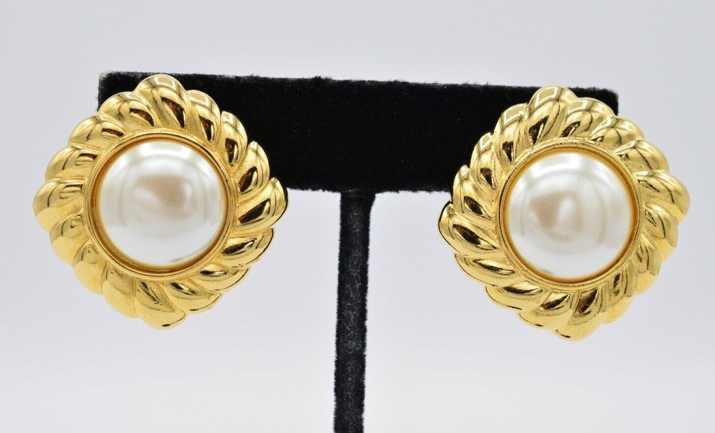 View of a pair of vintage gold Monet clip on earrings with pearls in the center