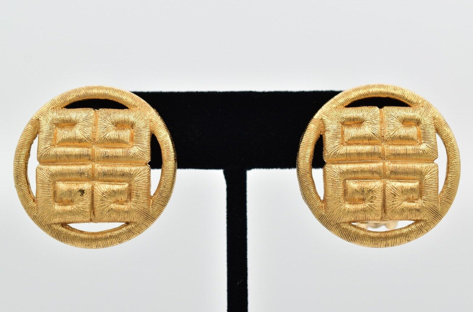 Pair of gold earrings on a black stand against a light gray background