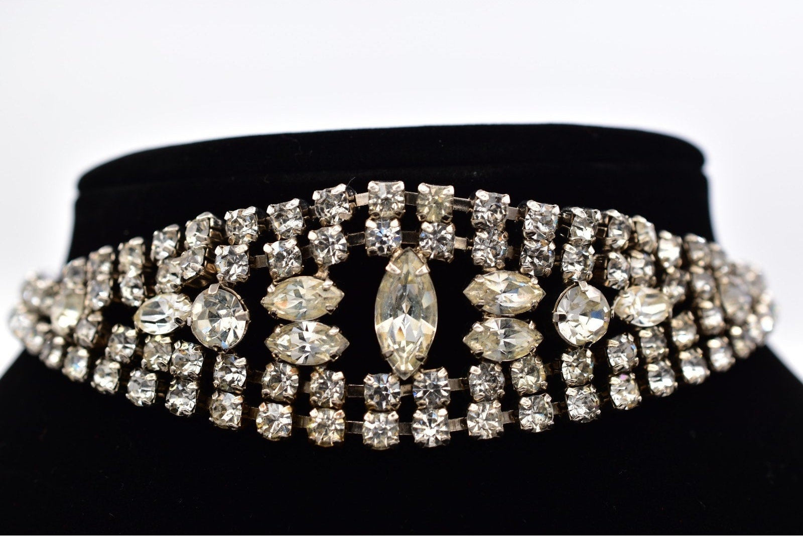 Decorative choker with crystals on a black stand against a white background