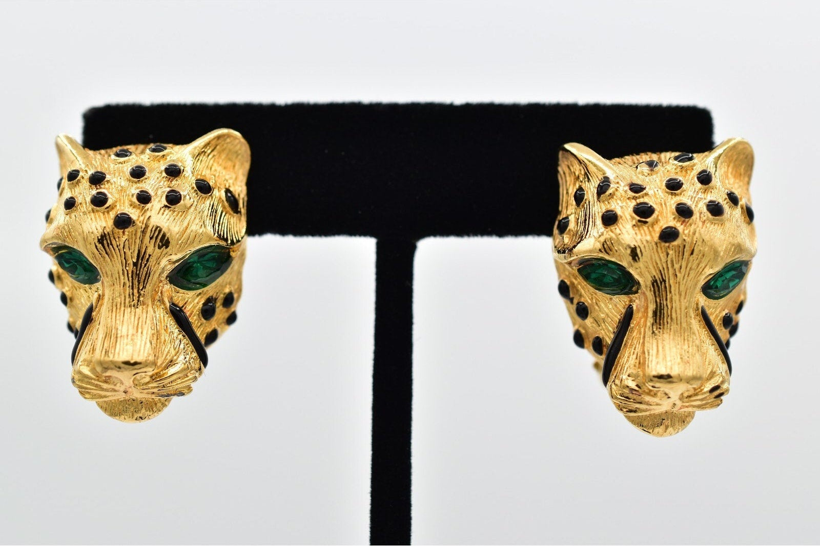 Gold panther head earrings with green eyes on a black and white background