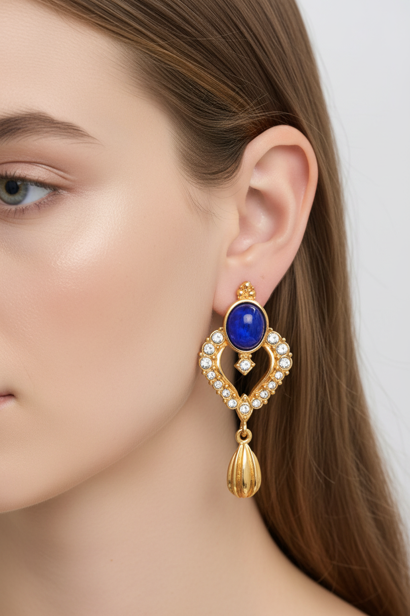 Gold earring with a blue gemstone worn by a model on a white background