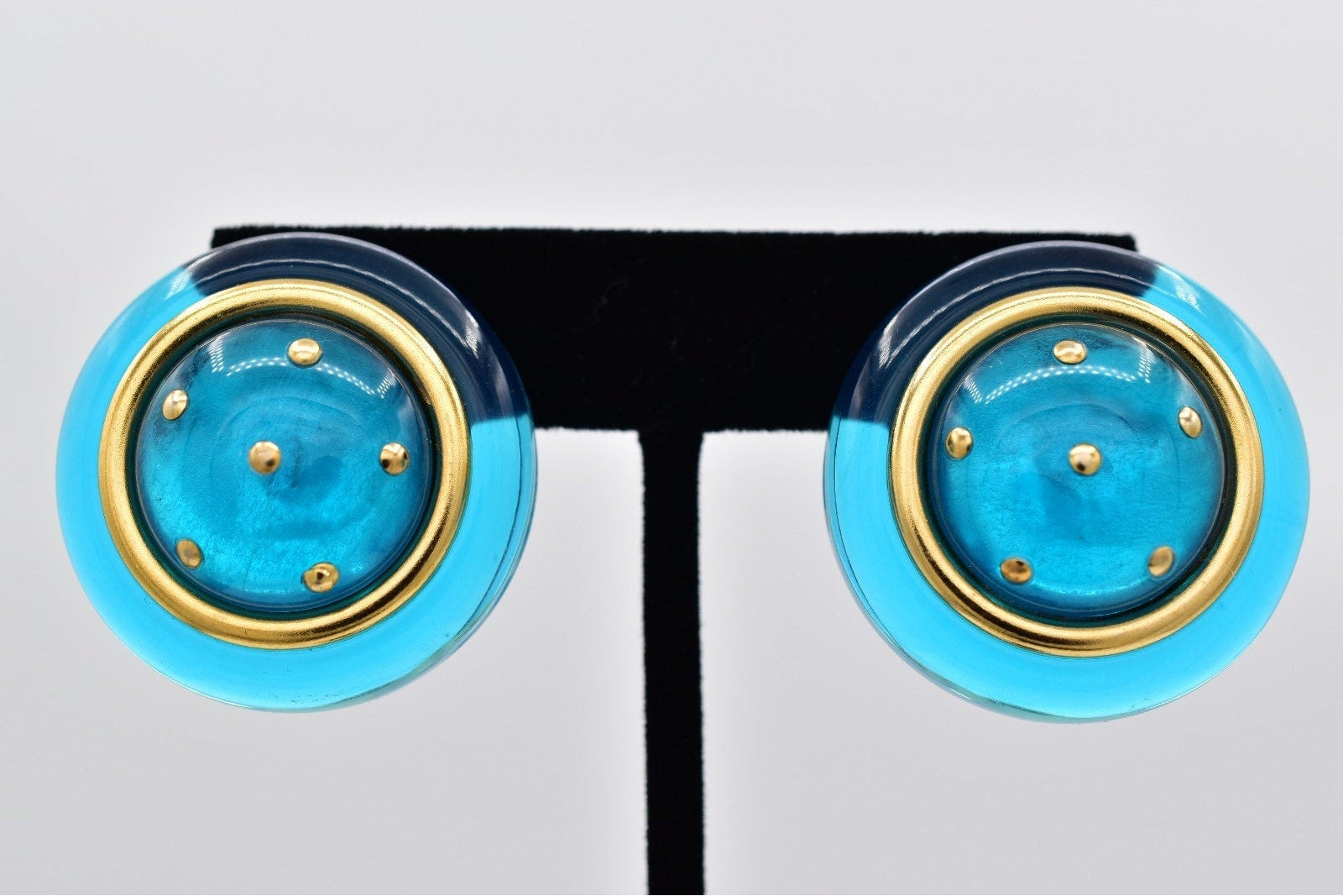 Pair of blue and gold circular earrings on a black stand against a light gray background