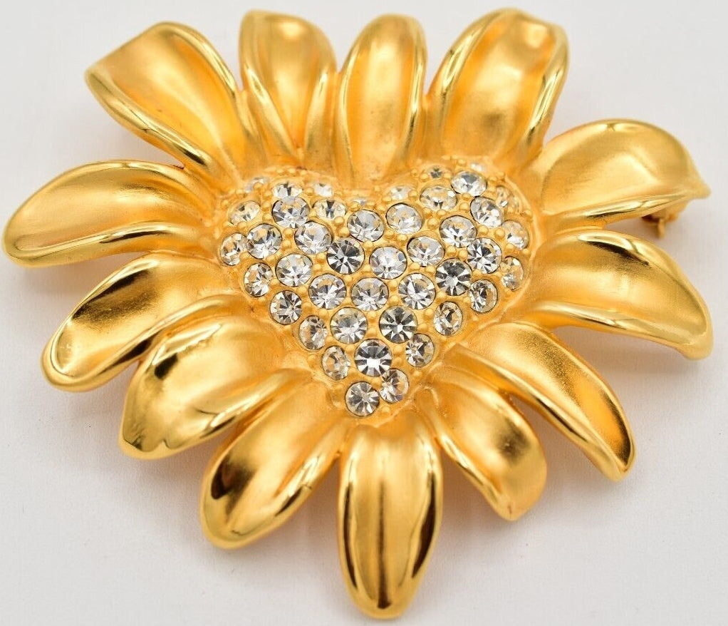 Gold Givenchy flower-shaped brooch with a heart center and clear stones on a white background