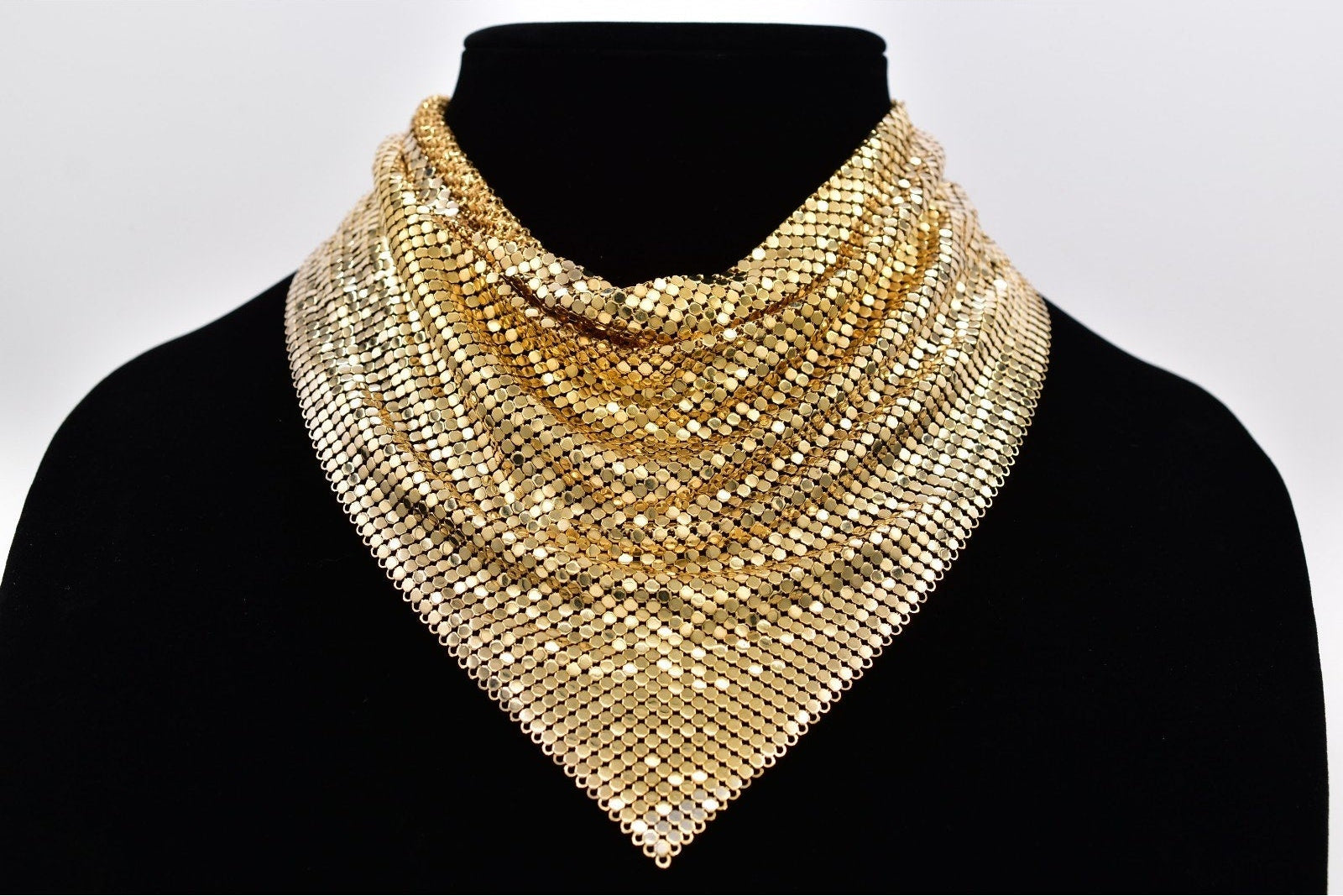 Gold mesh necklace on a black mannequin against a white background