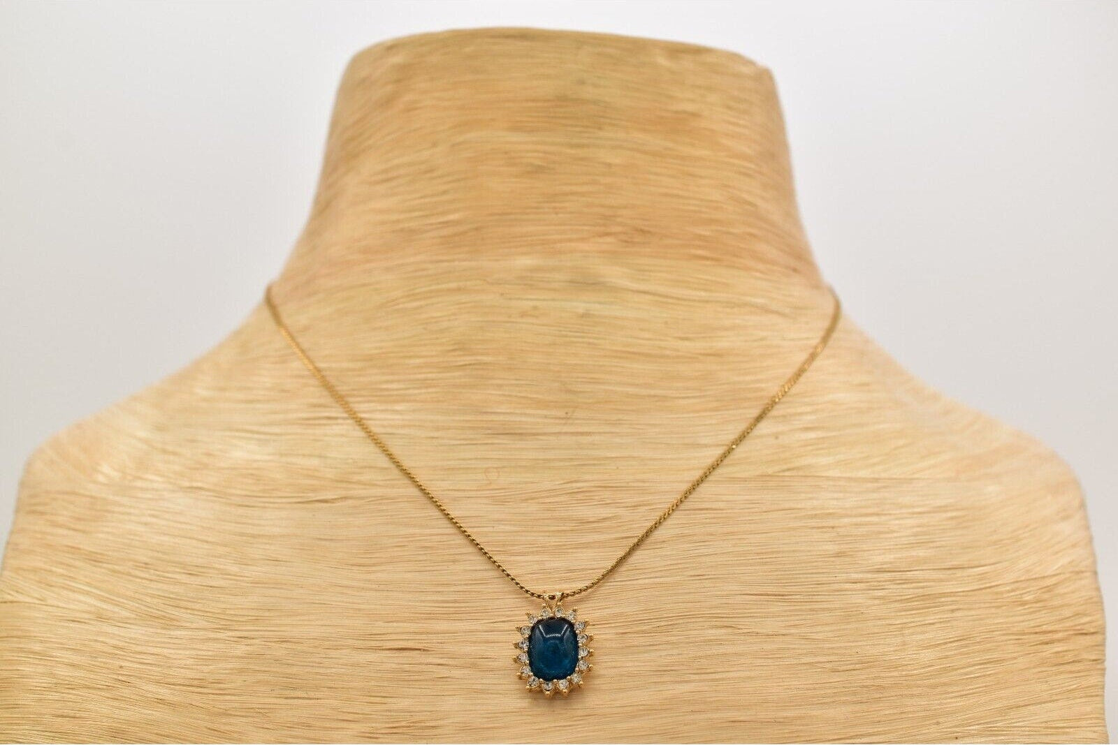 Gold necklace with a blue pendant on a mannequin neck.