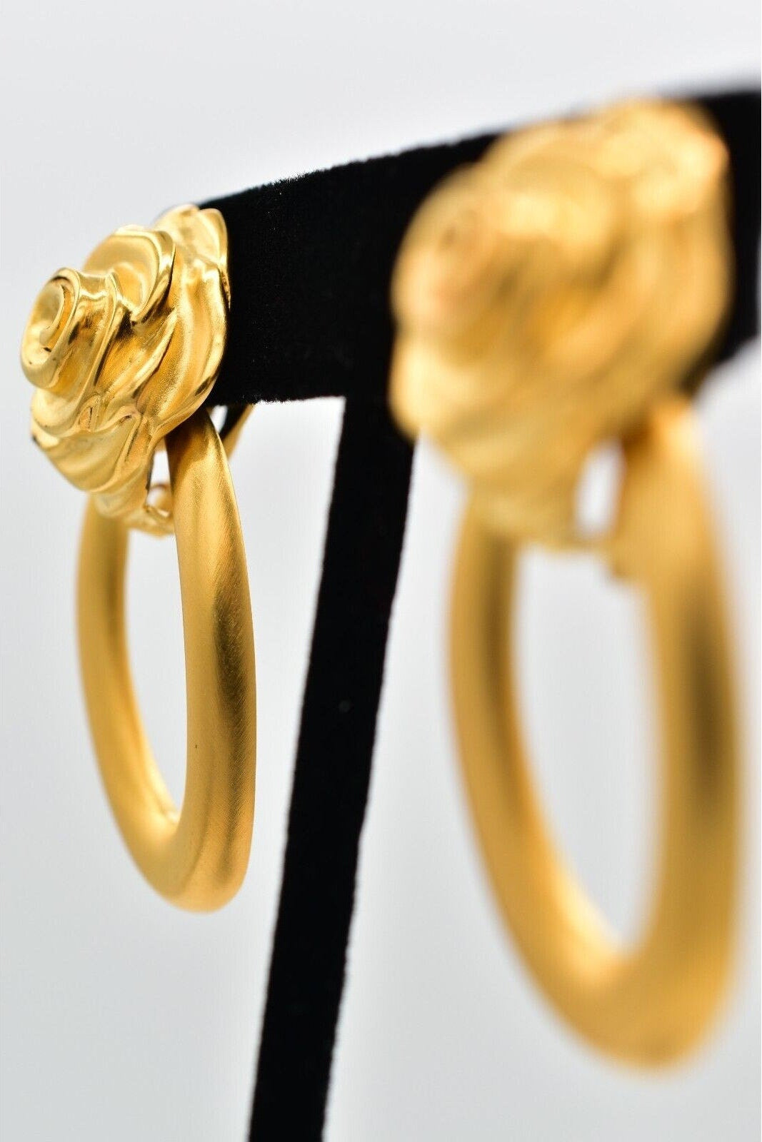 Gold hoop earrings on a black stand against a white background
