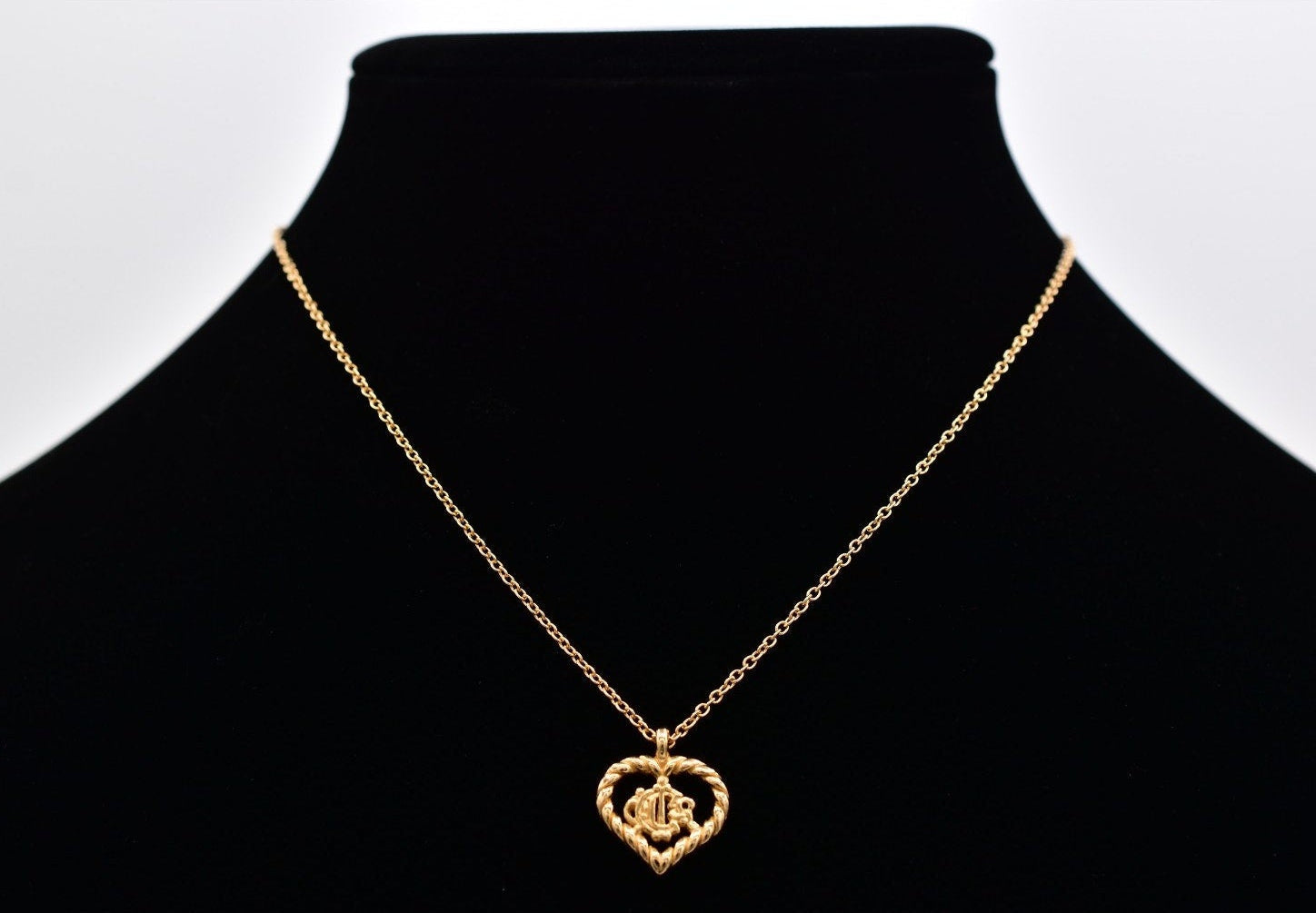 Gold necklace with a heart-shaped pendant on a black mannequin bust against a white background