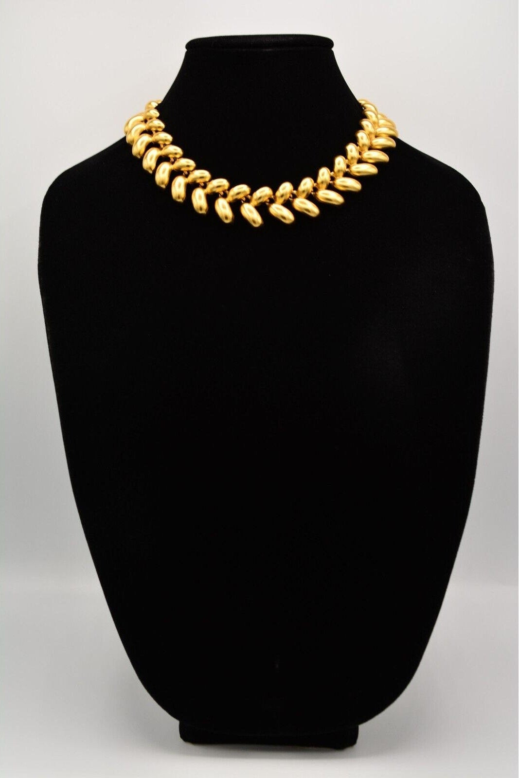 Gold necklace on a black mannequin bust against a white background