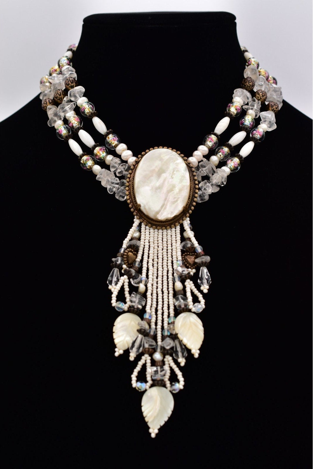 Decorative necklace with shell and bead details on a black mannequin against a white background