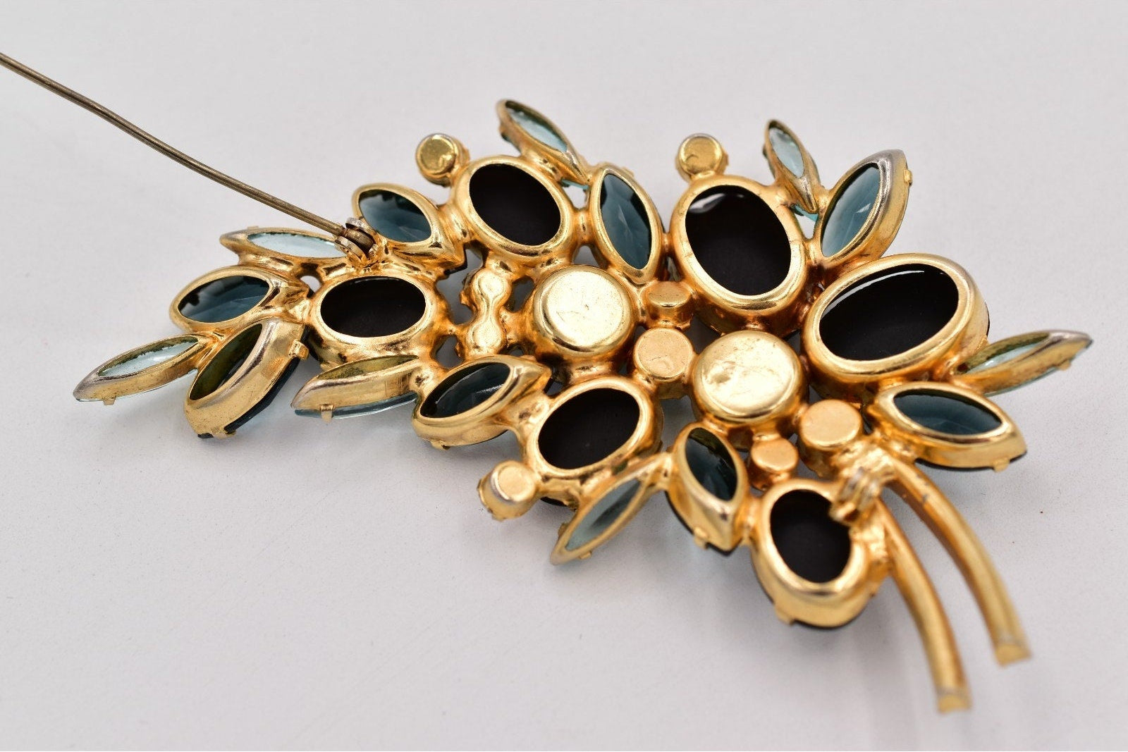 Gold brooch with black and green gemstones on a light gray background