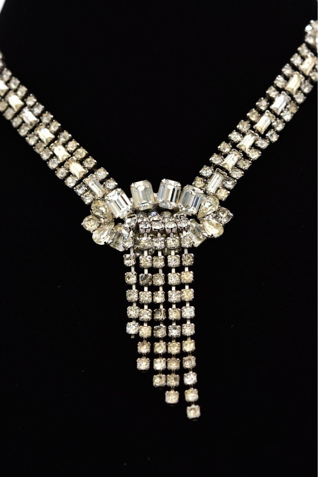 A silver-tone rhinestone necklace with a wide collar-style top and cascading fringe drops, displayed on a black background.