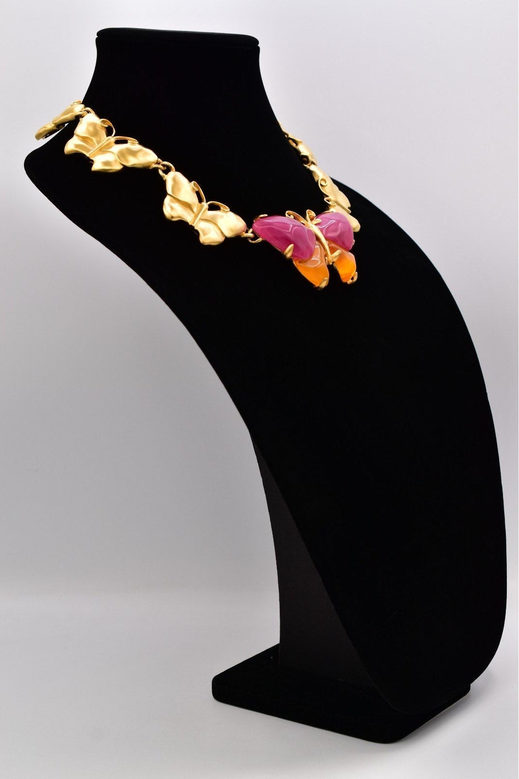 Side view of vintage Givenchy gold butterfly necklace with pink and orange lucites on a black mannequin against a white background.