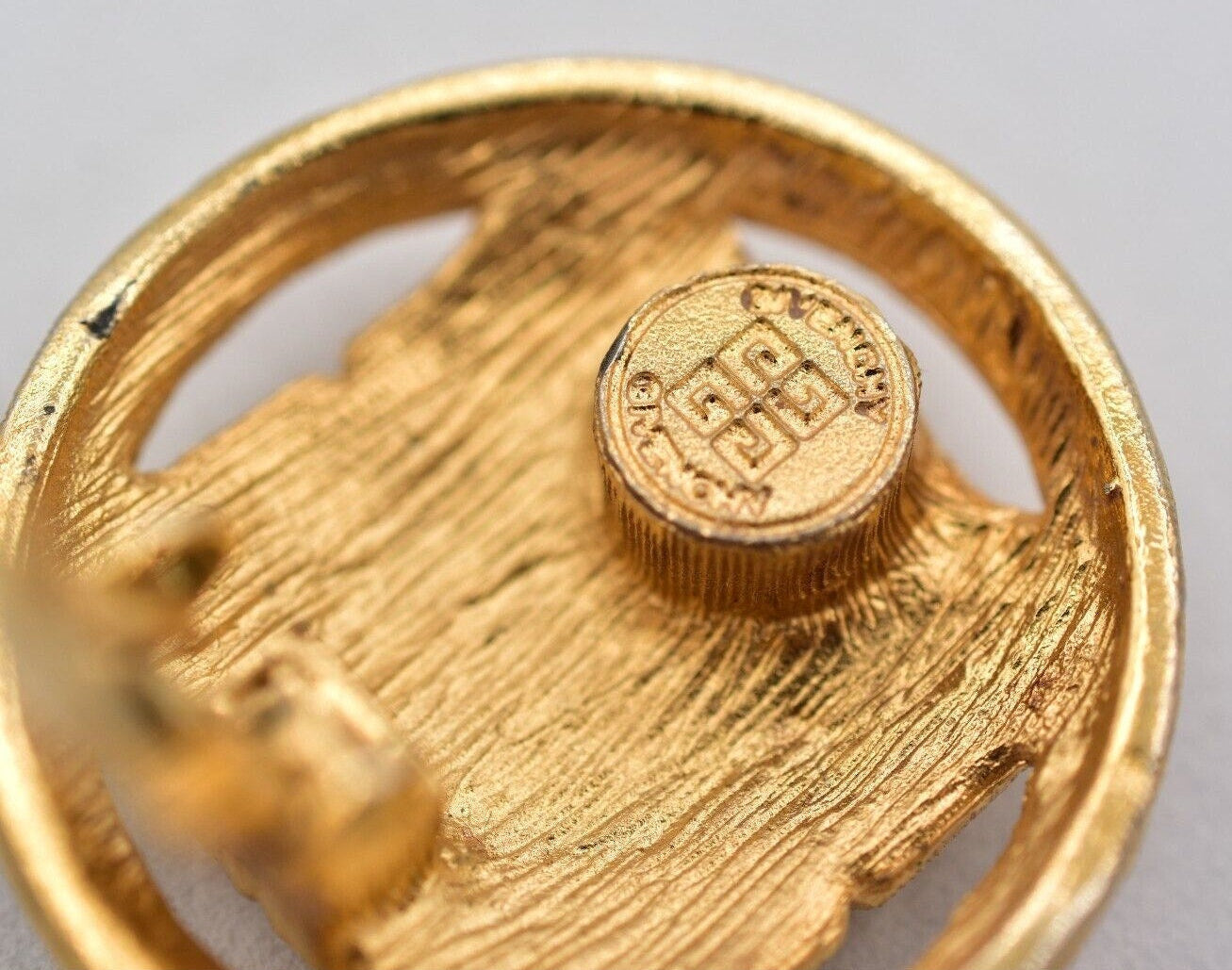 Close-up of a gold earring with a visible hallmark on a gray background