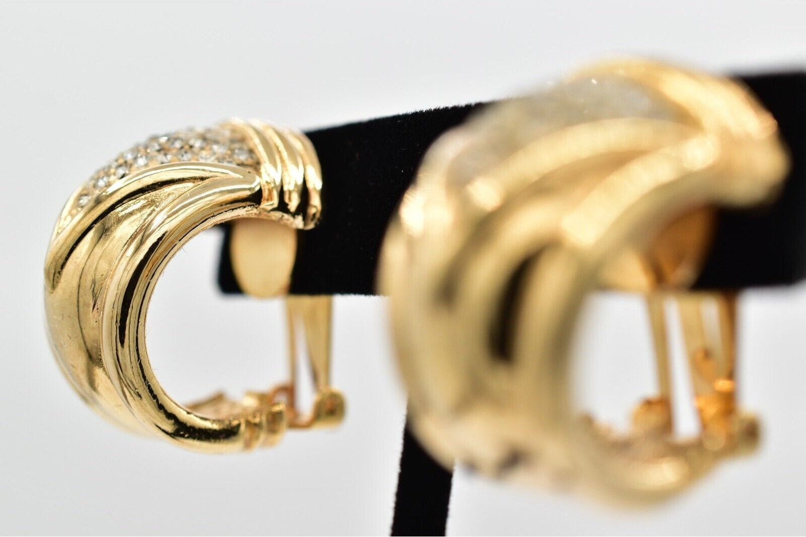 Gold hoop earrings on a black stand against a white background