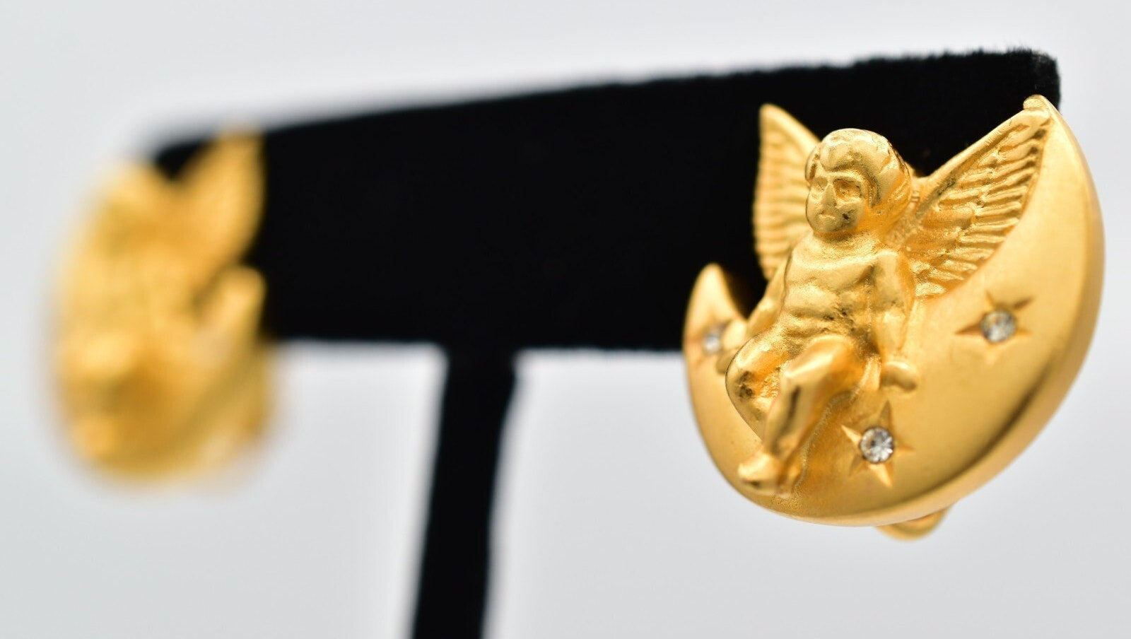 Gold angel earrings on a black earring stand with a light gray background