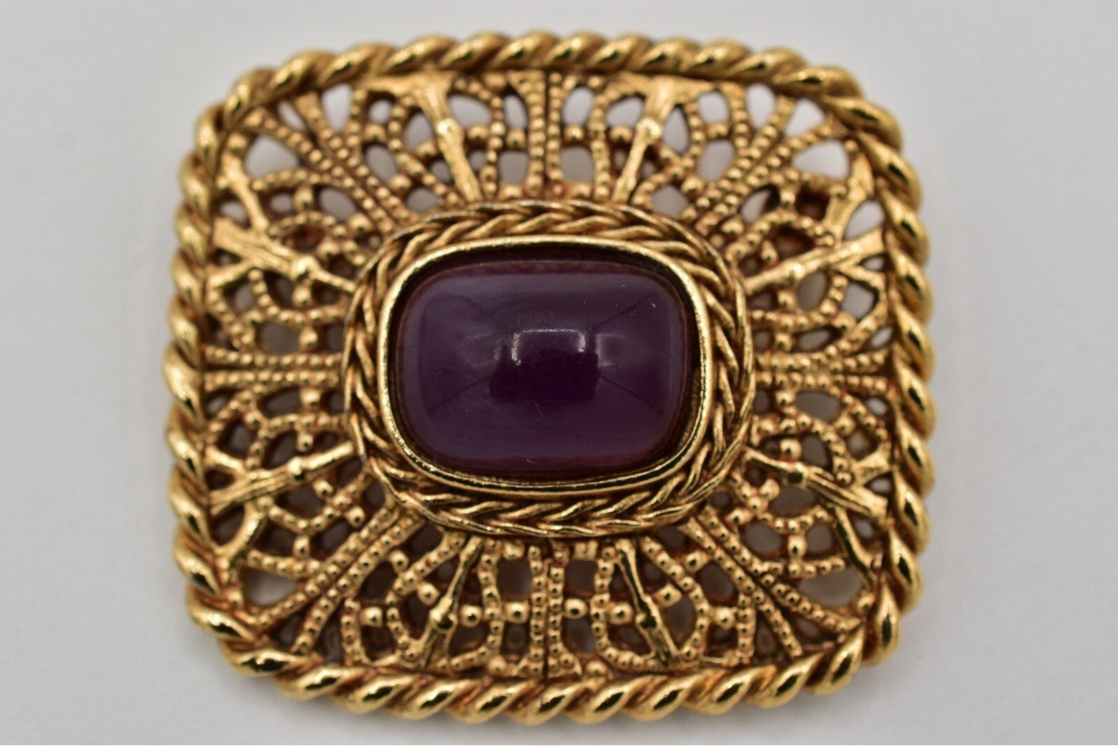 Gold brooch with a purple gemstone on a gray background