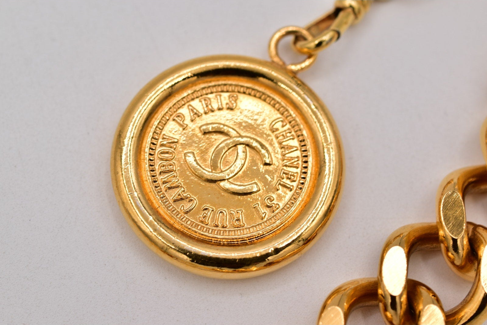 Gold Chanel necklace with a round pendant on a light gray background