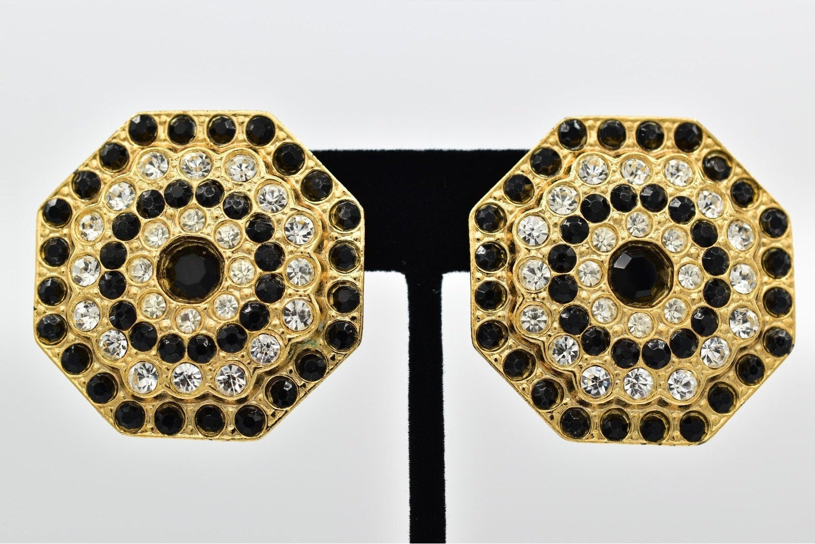 Hexagonal earrings with gold, black, and clear gemstones on a white background