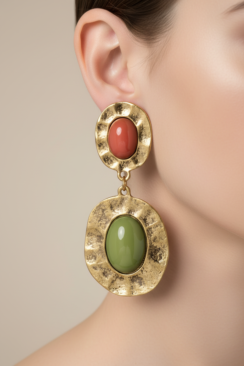 A pair of vintage chunky dangle earrings with green and orange lucite cabochons in an antiqued gold setting, displayed on a black stand.