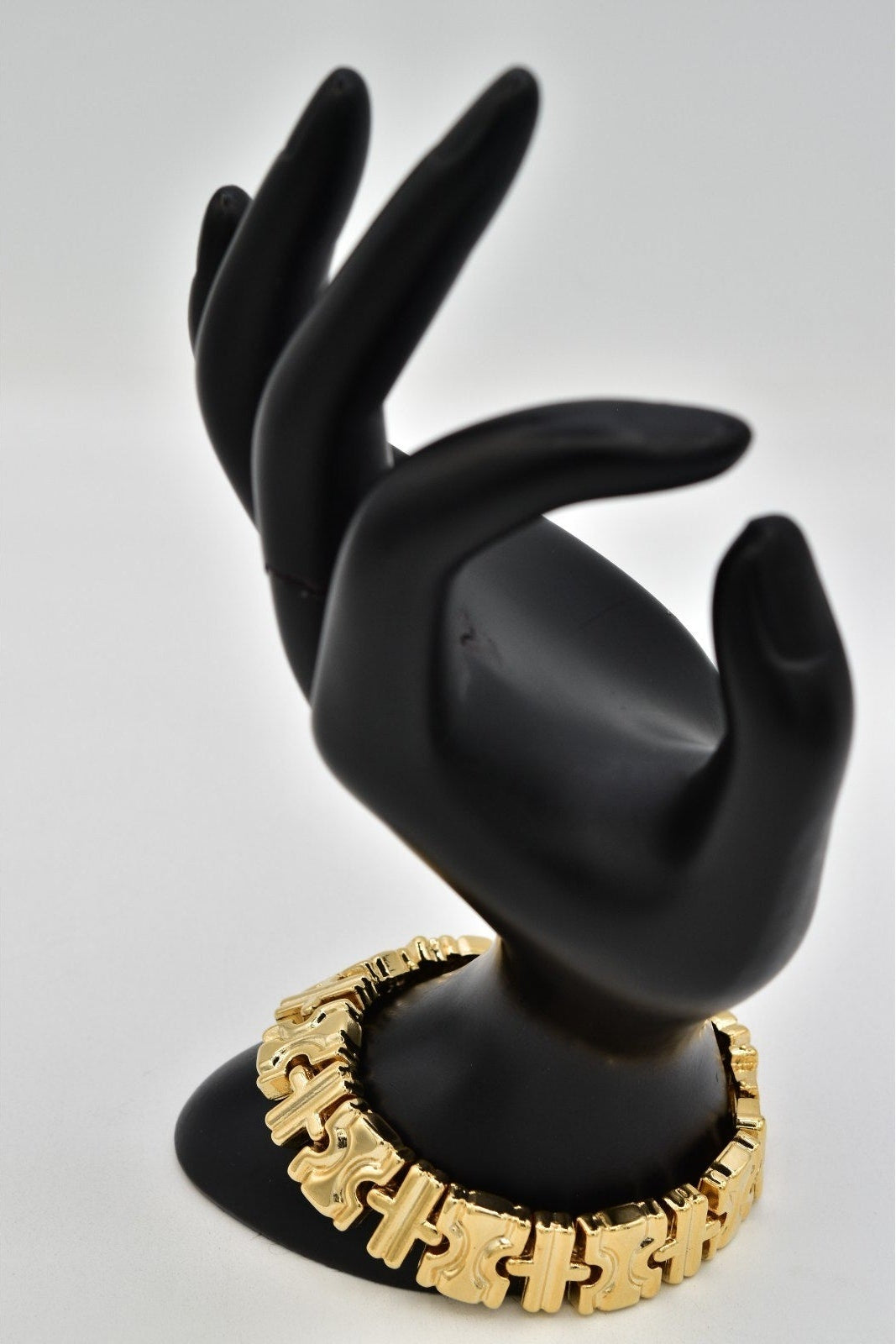 A gold-tone chain bracelet displayed on a black hand-shaped jewelry stand against a light gray background.