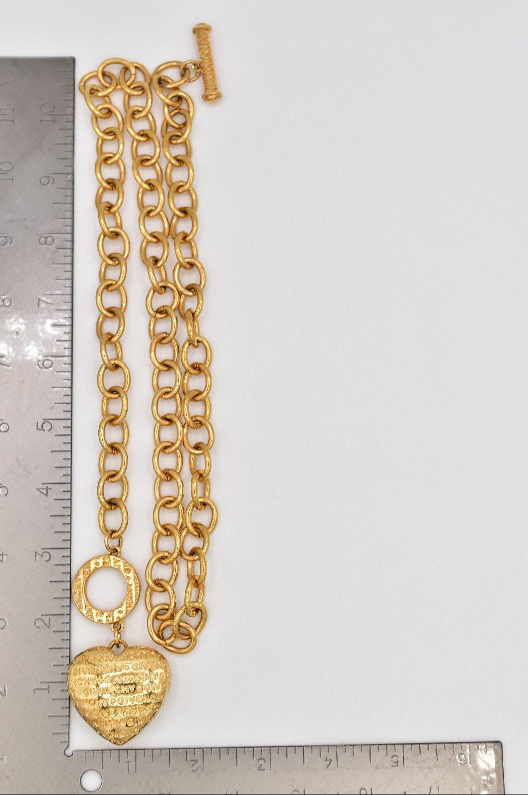 Gold chain necklace with a heart-shaped pendant on a white background with a ruler for scale.