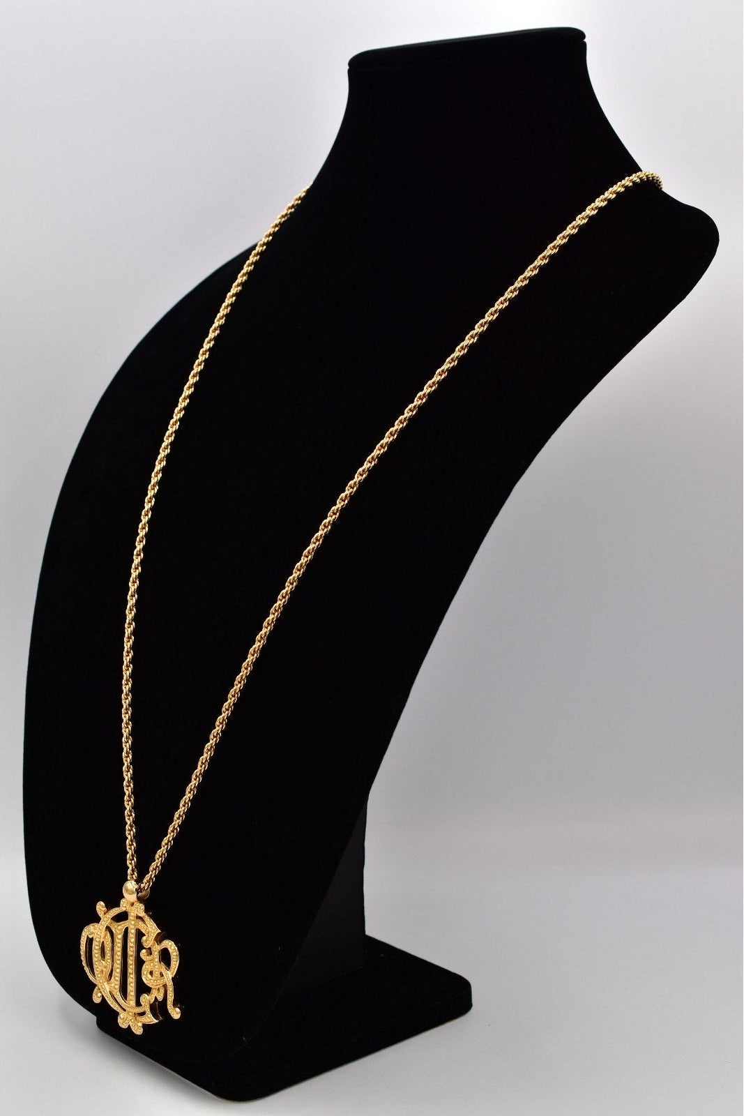 Gold necklace with a pendant on a black mannequin bust against a white background