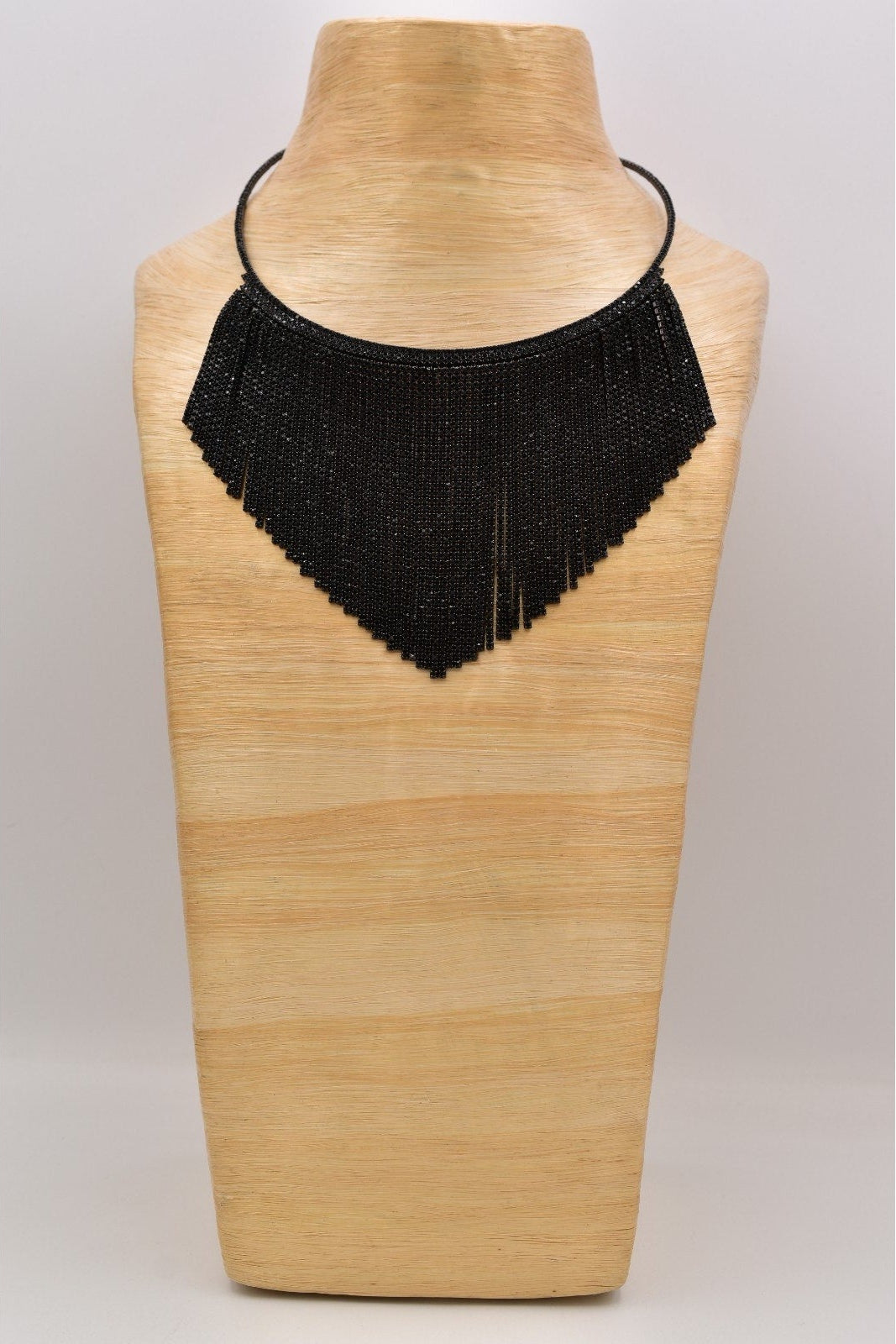 Black beaded necklace on a wooden mannequin bust against a light gray background