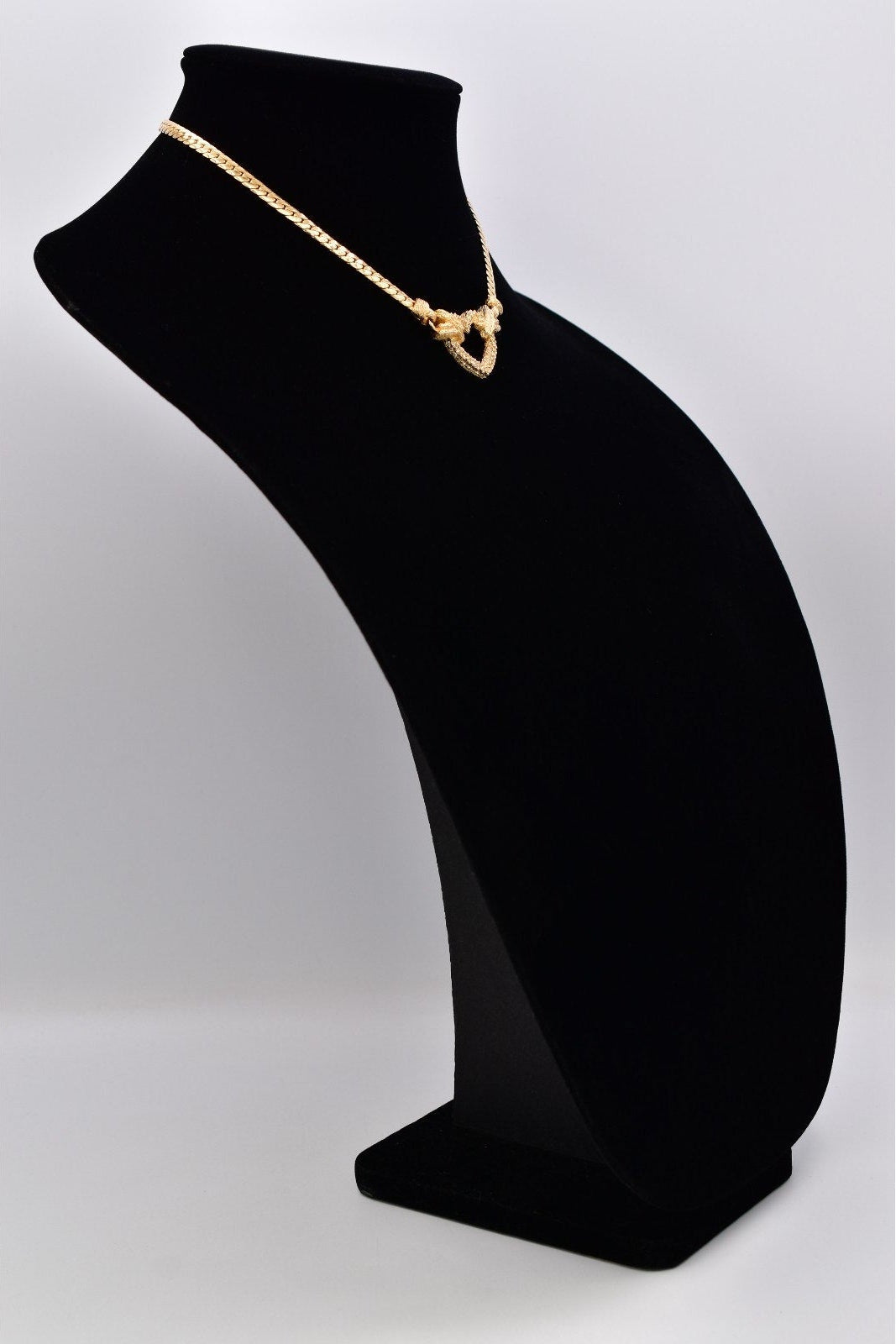 A gold necklace displayed on a black velvet jewelry bust against a light gray studio background.