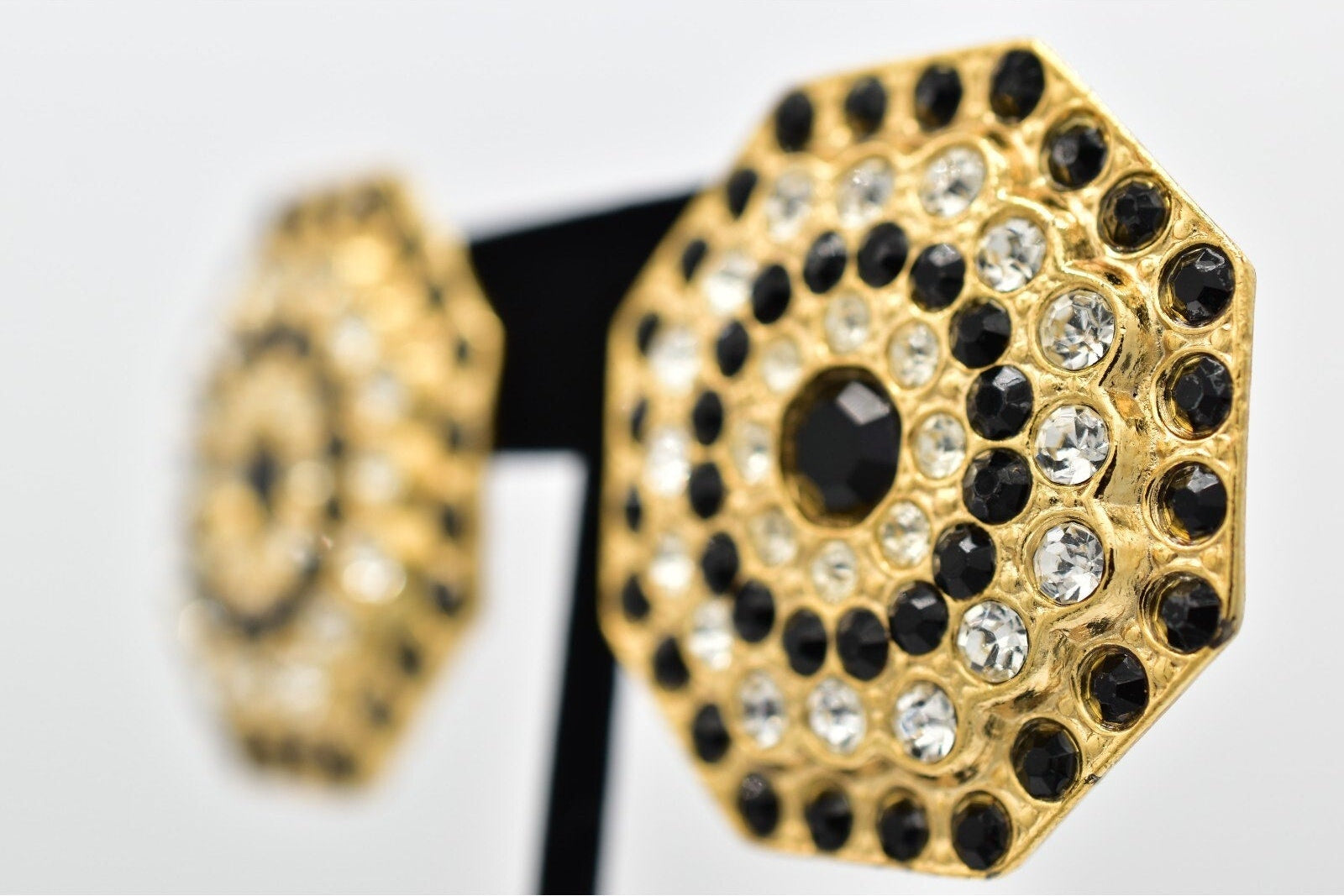 Gold and black embellished earrings on a stand with a white background