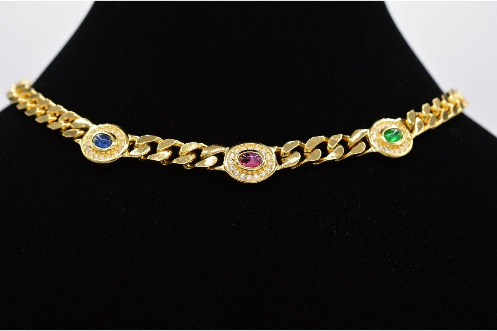 Gold chain bracelet with embedded gemstones on a black stand