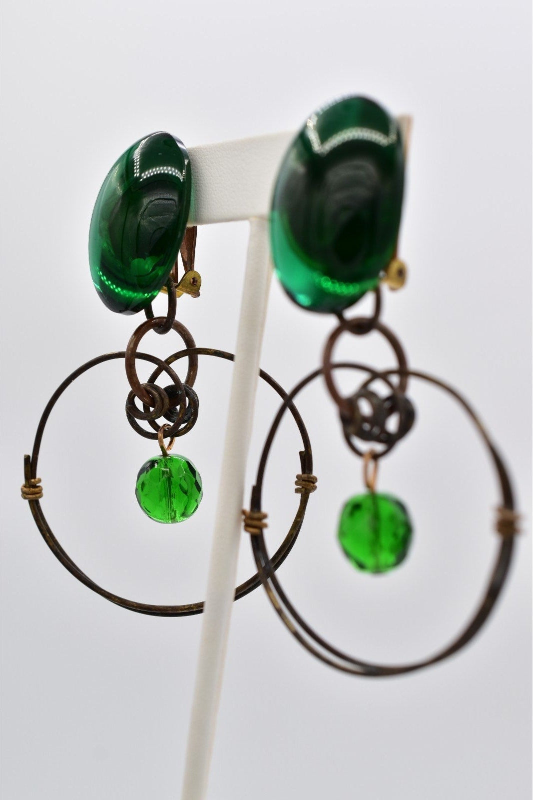 Pair of green earrings on a white stand against a light gray background