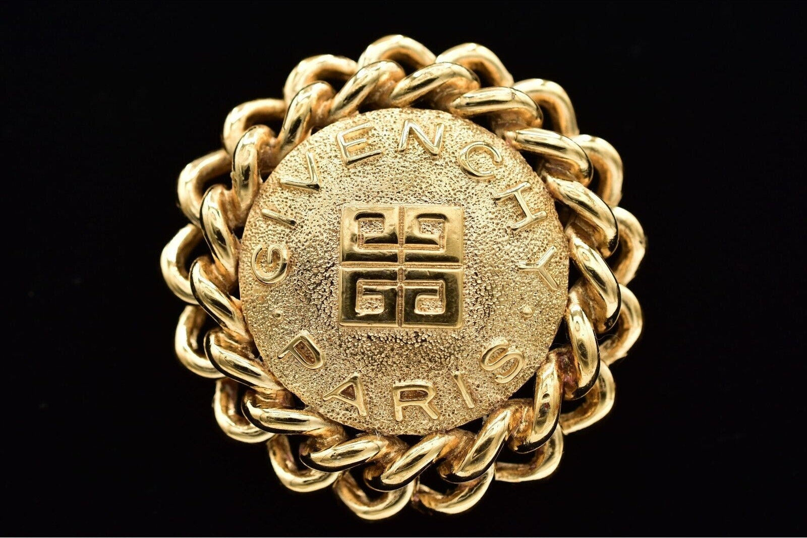 Gold brooch with intricate design and brand name on a black background