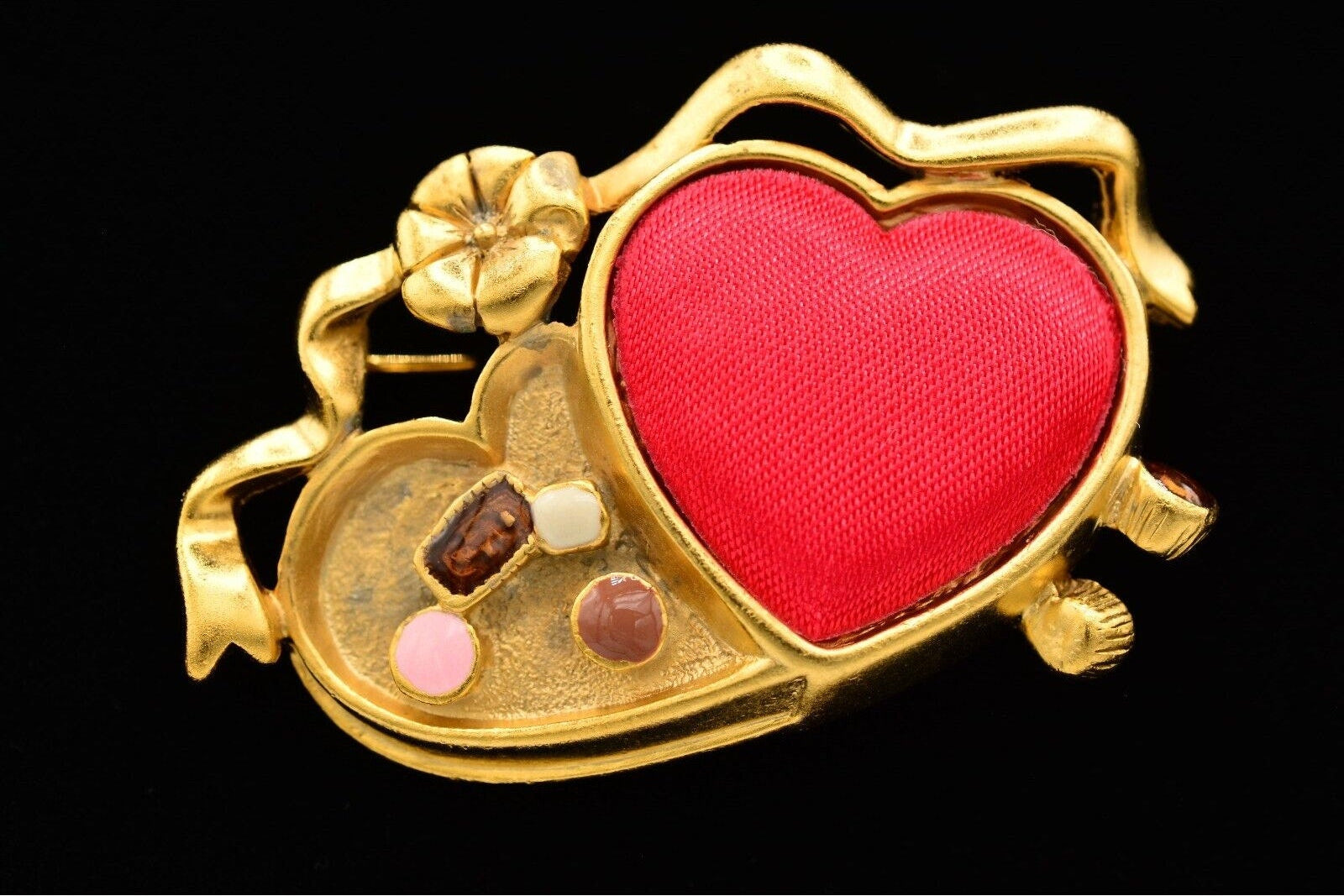 Gold brooch with red heart and embedded stones on a black background