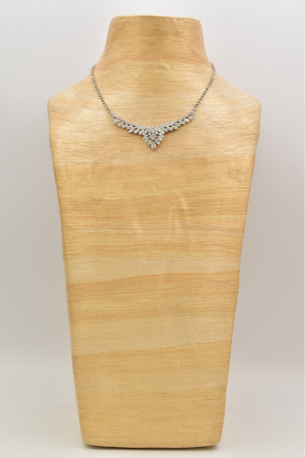 Silver necklace on a wooden mannequin bust against a plain background