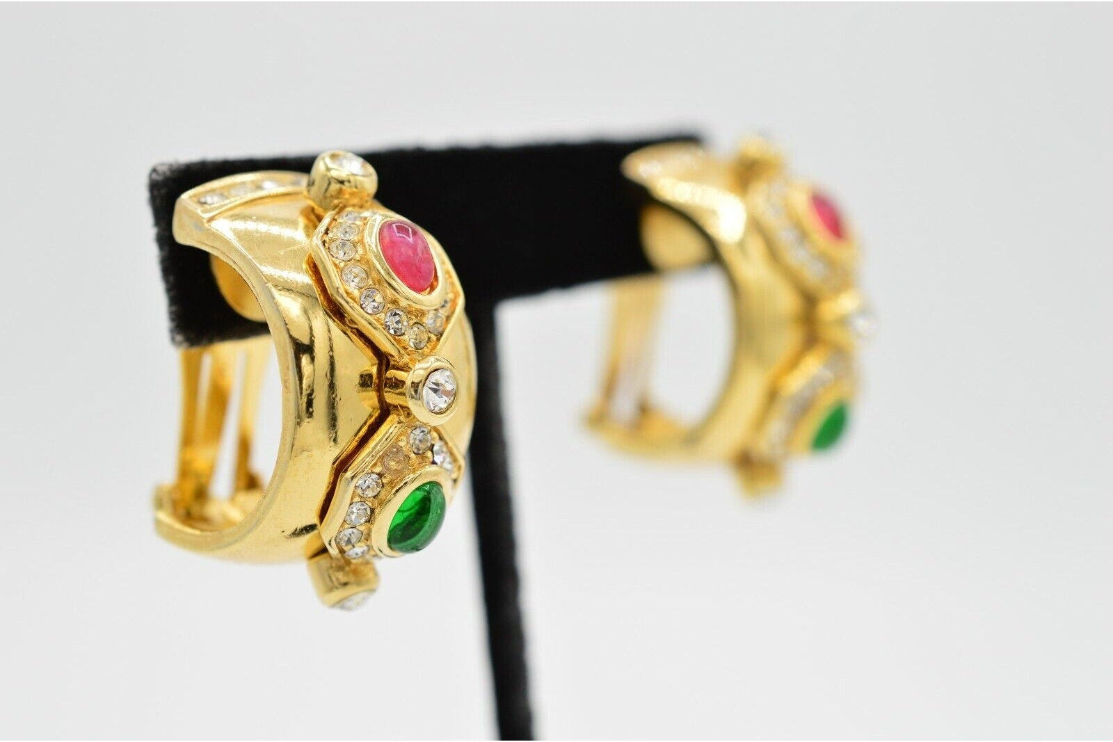 Gold hoop earrings with gemstones on a black stand against a light gray background