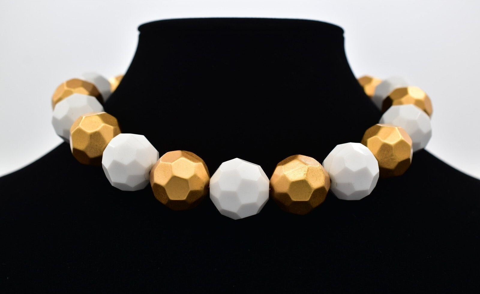 Necklace with gold and white beads on a black mannequin against a white background