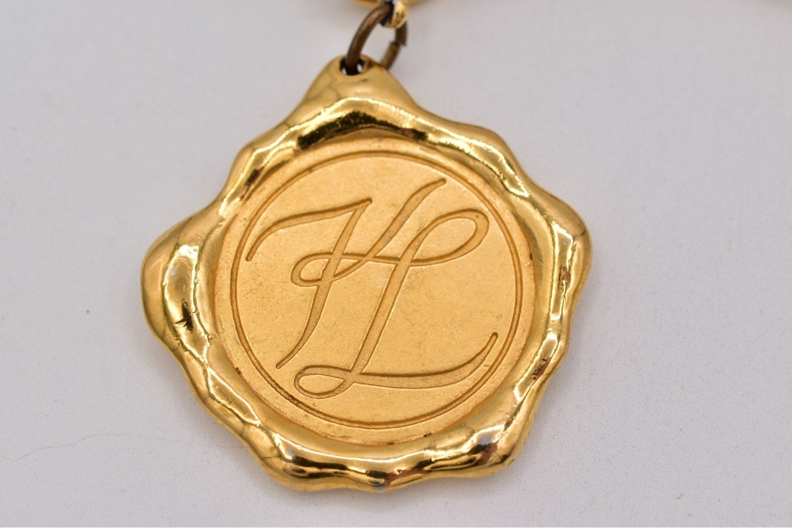 Gold pendant with initials 'KL' on a gray background