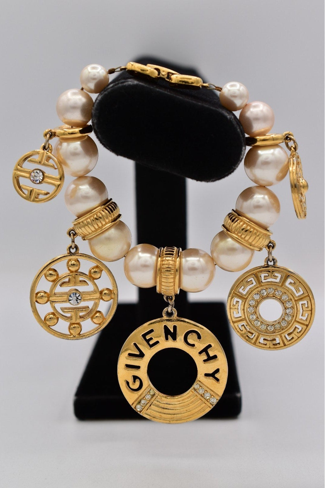 Gold and pearl bracelet with Givenchy logo on a black stand against a gray background