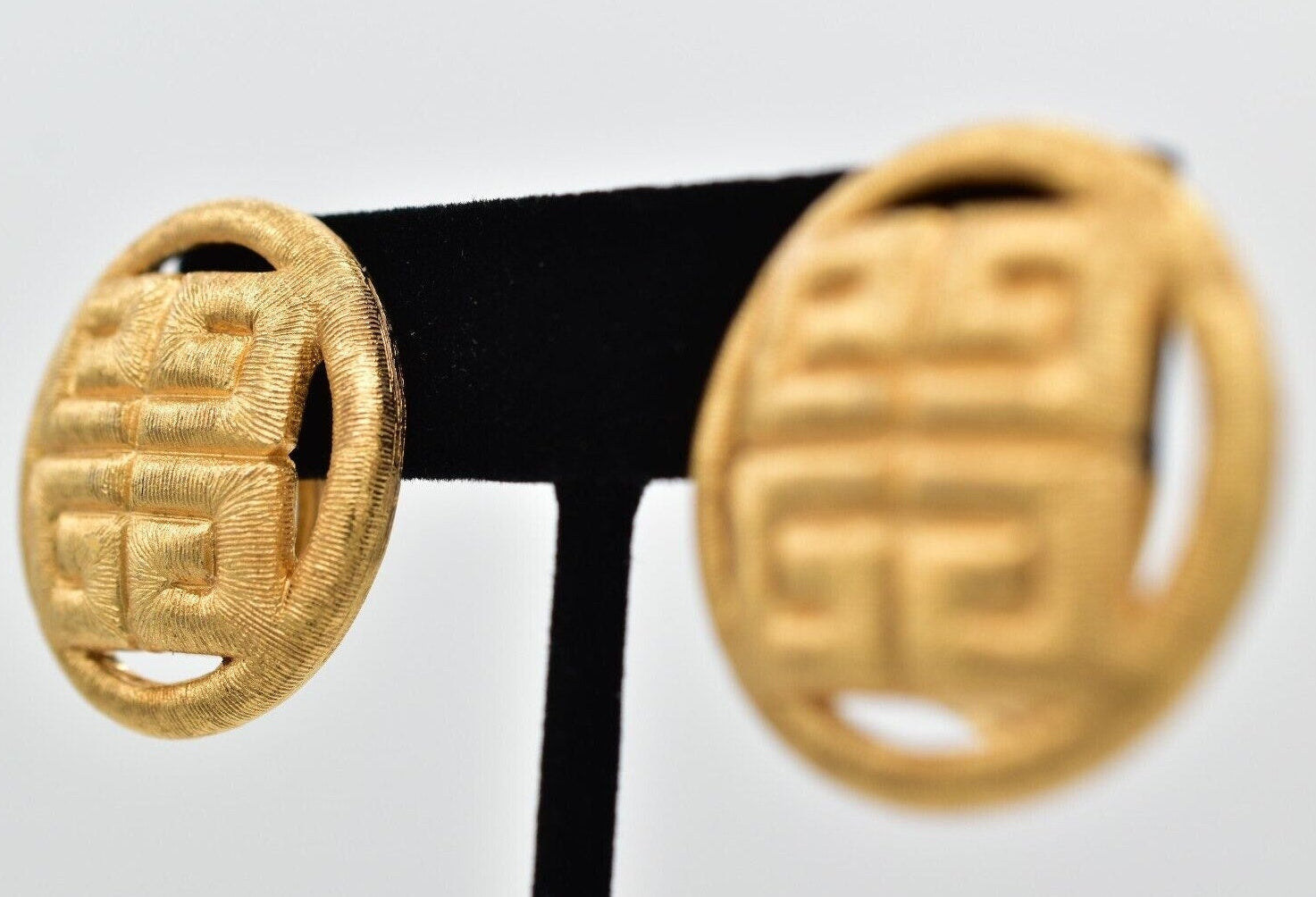 Pair of gold earrings on a black stand against a light gray background