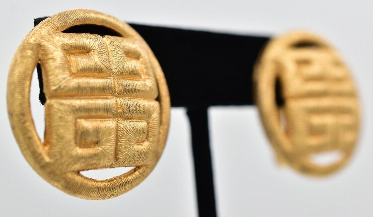 Gold earrings on a black stand against a white background