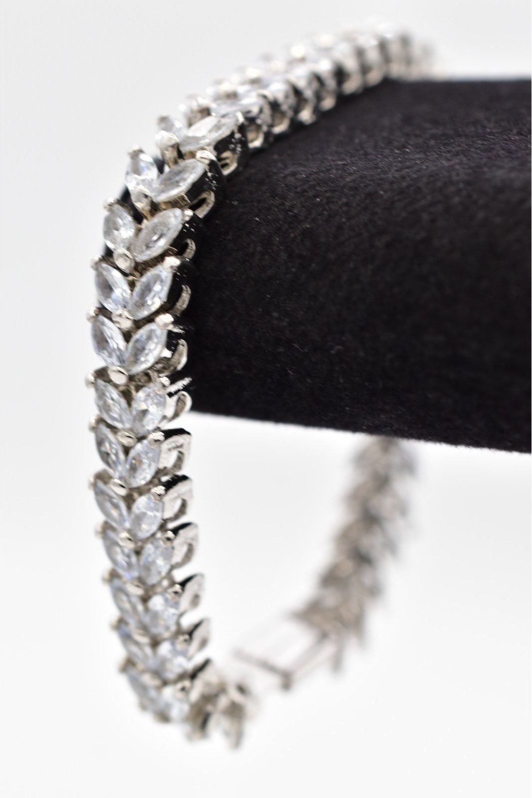 Silver bracelet with clear stones on a black stand against a white background