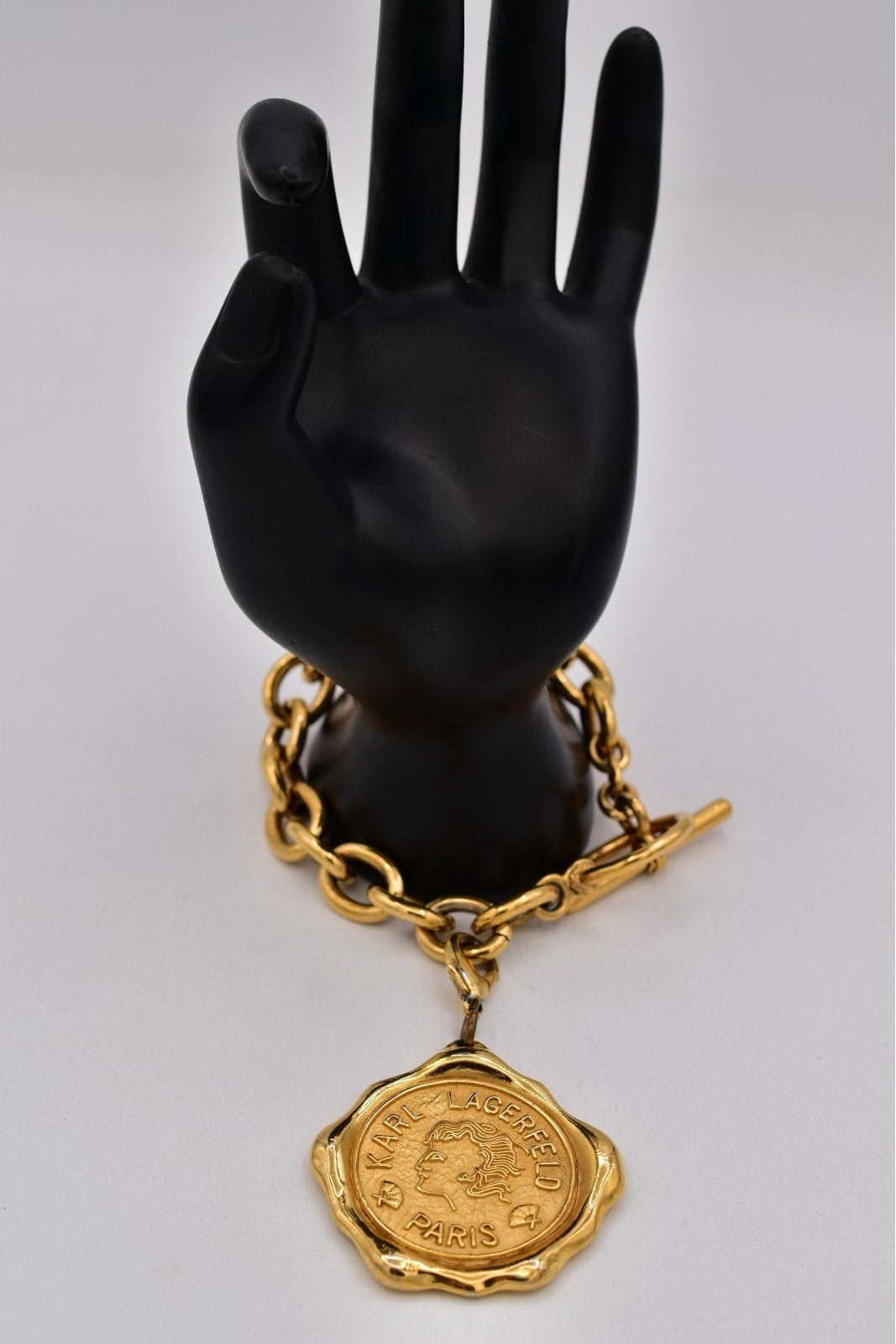 Gold chain bracelet with a medallion on a black mannequin hand against a white background