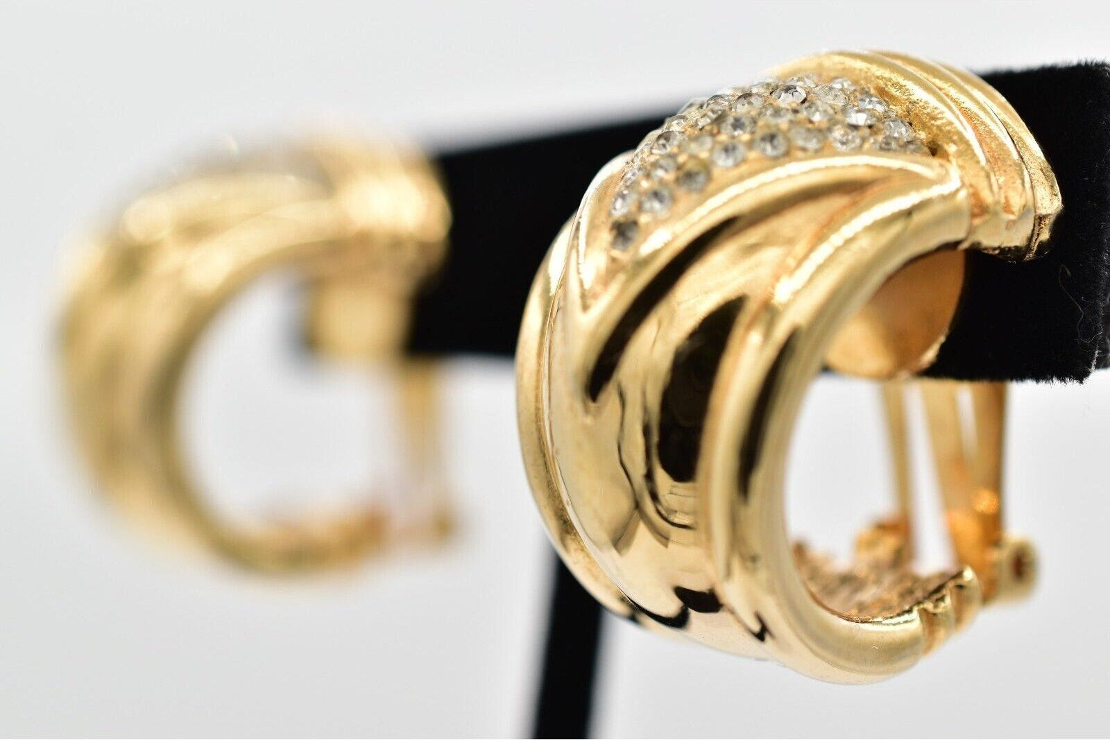 Gold hoop earrings with clear stones on a black stand against a white background