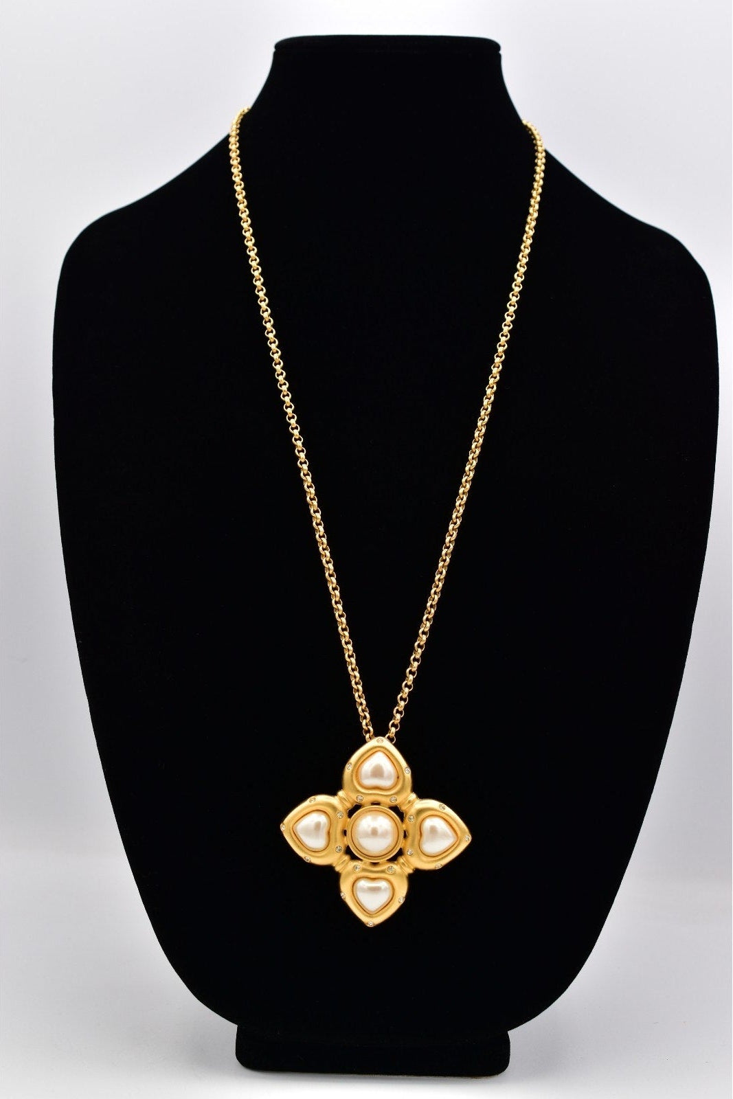 Gold necklace with a floral pendant on a black bust against a white background